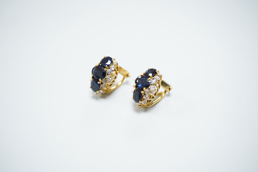 A pair of sapphire earrings, each set with three oval sapphires, within a border of brilliant-cut cubic zirconias, mounted in gold, length 1.4cm each, clip and retractable post fittings
